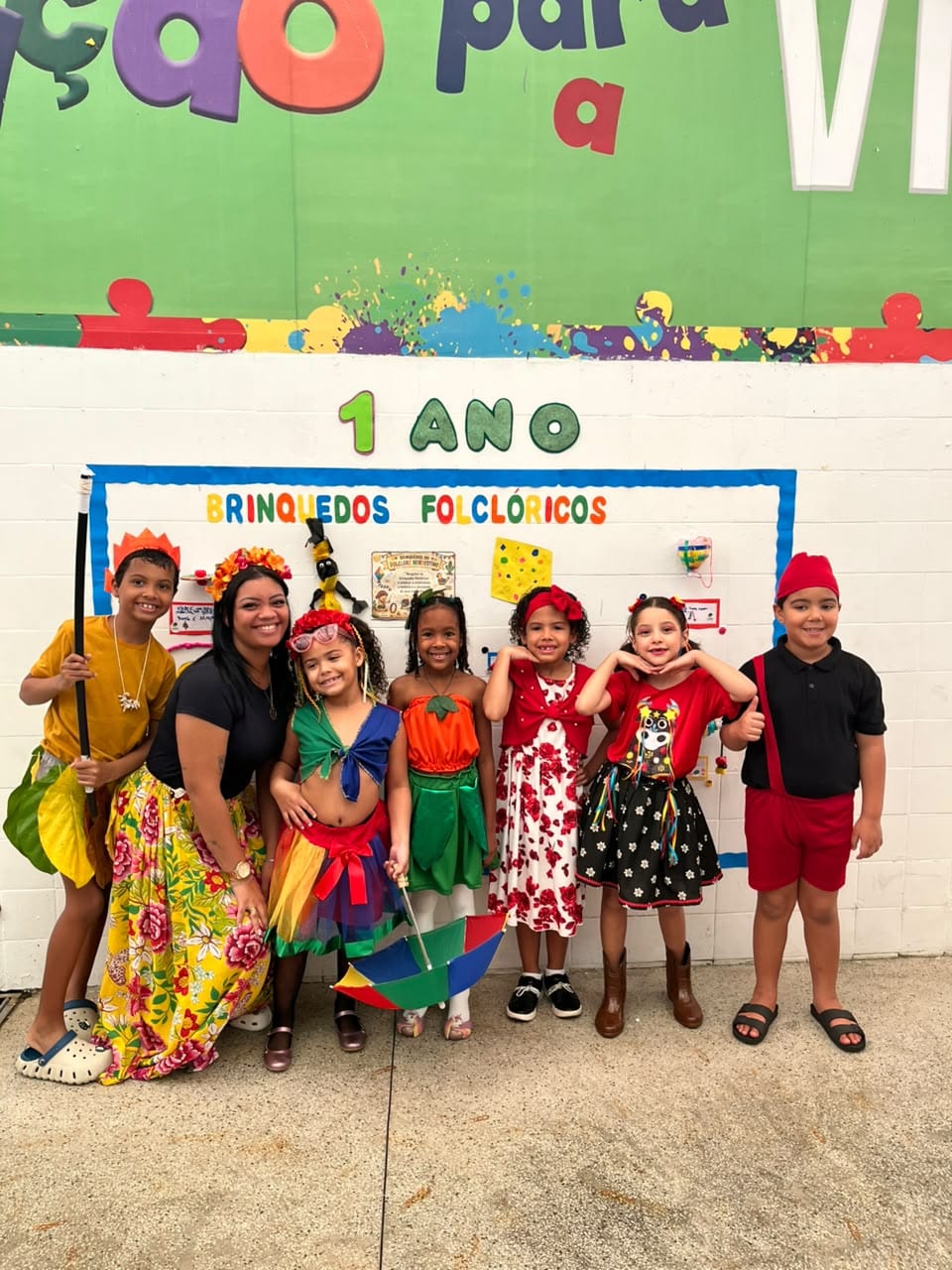 Professora e crianças do 1º ano em frente ao painel da turma