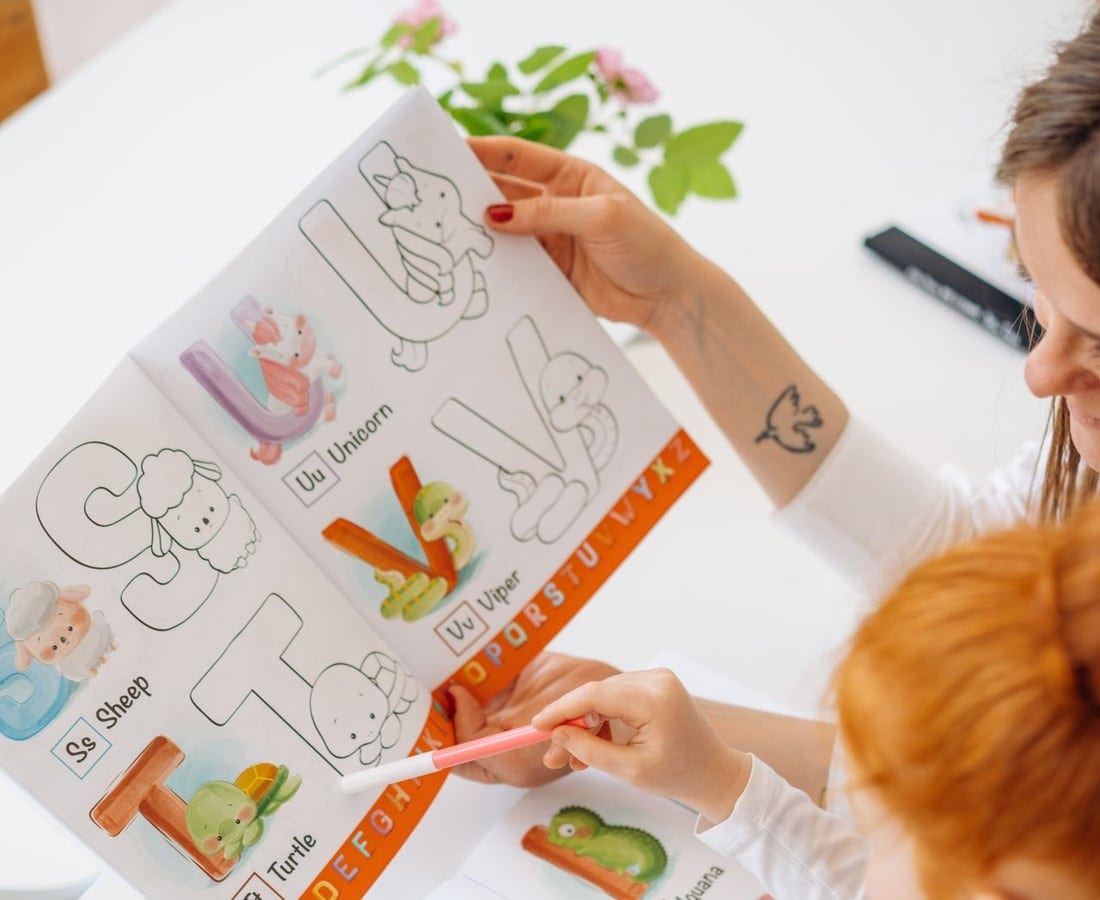 Caderno de alfabeto com palavras em inglês e mãos apontando as letras (imagem ilustrativa)