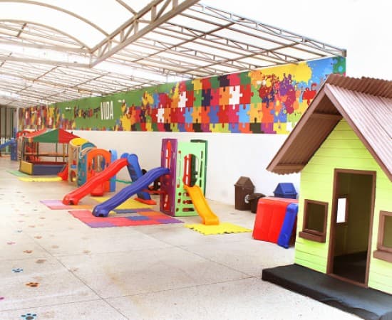 Pátio coberto com casinha de brinquedo, escorregadores e painel colorido de quebra-cabeça na parede