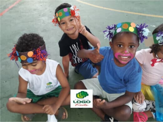 Três crianças sentadas no pátio usando coroas de carnaval coloridas
