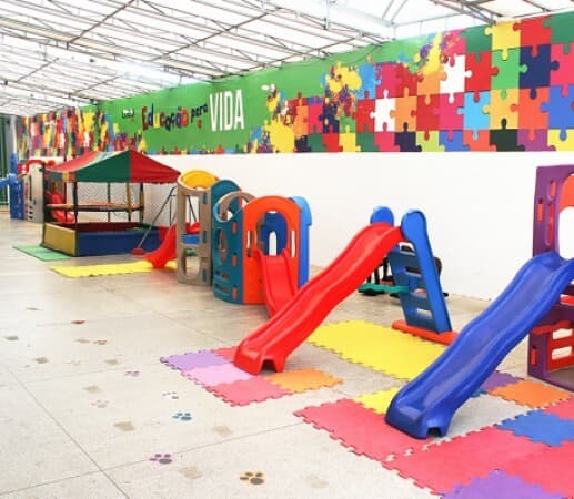 Espaço de recreação com escorregadores vermelho e azul sobre piso emborrachado