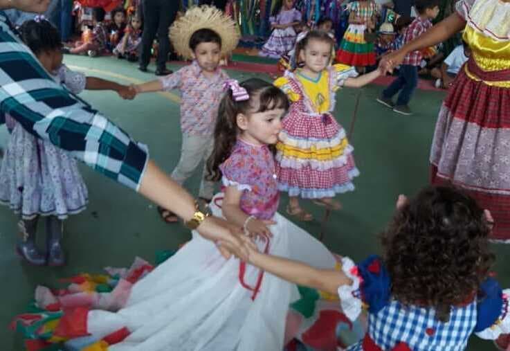 Crianças e professoras dançando quadrilha de mãos dadas no pátio