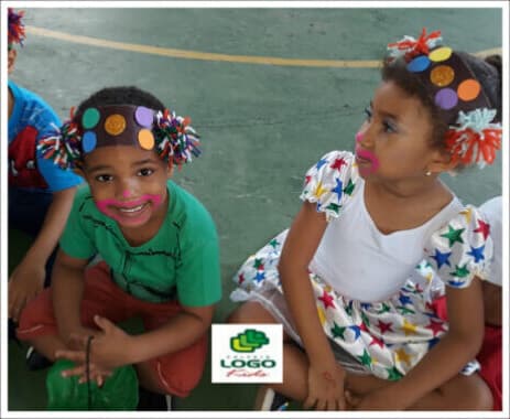 Dois meninos com adereços coloridos na cabeça, sentados na quadra