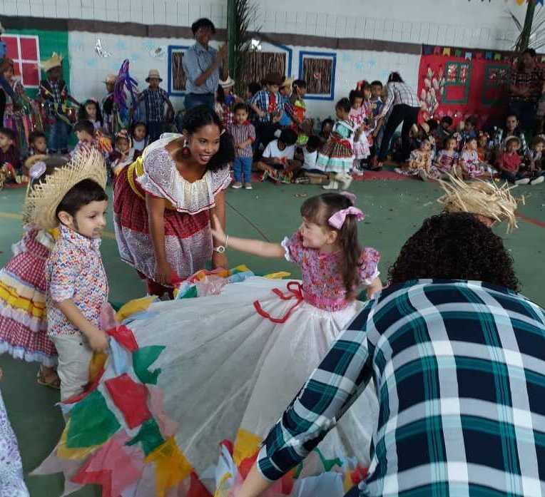 Roda de dança de festa junina, com crianças de vestido rodado e adultos acompanhando